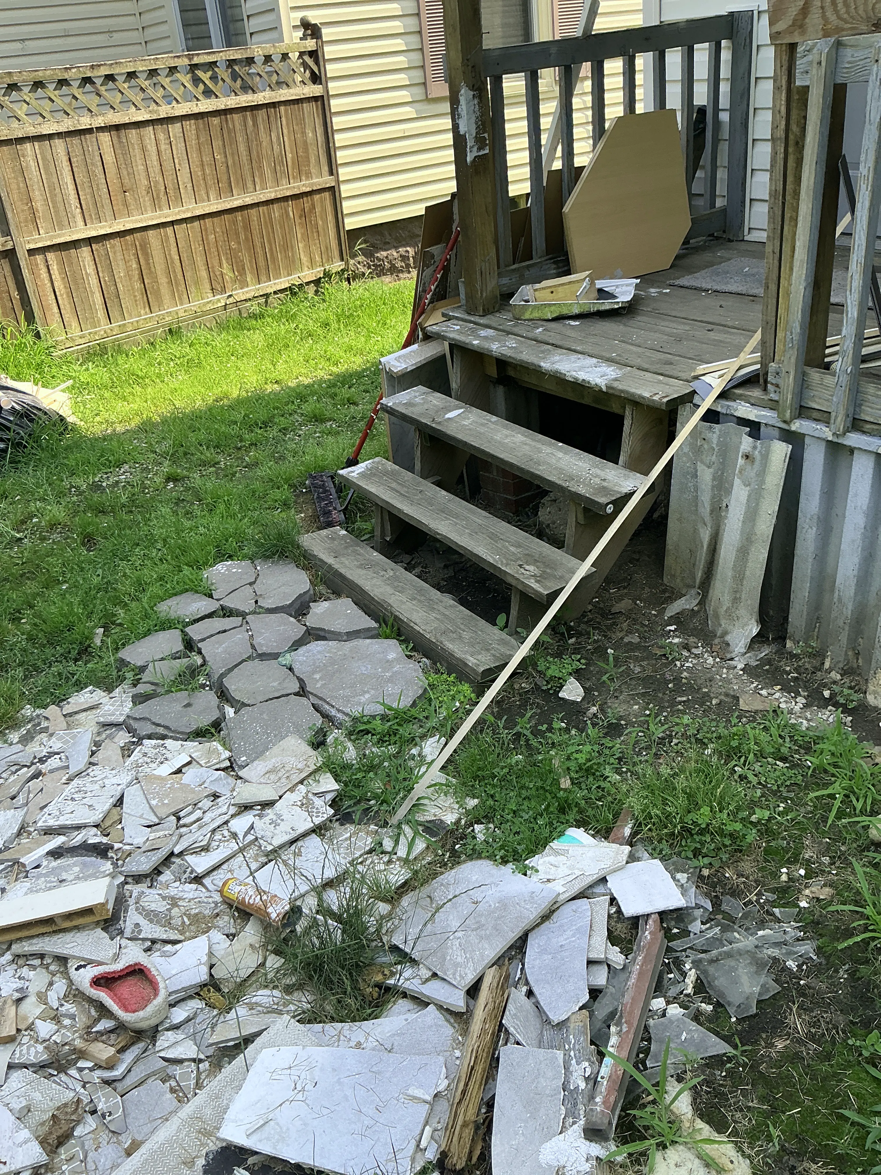 Cluttered yard with broken tiles and unsafe weathered wooden porch stairs. 2026-08-21