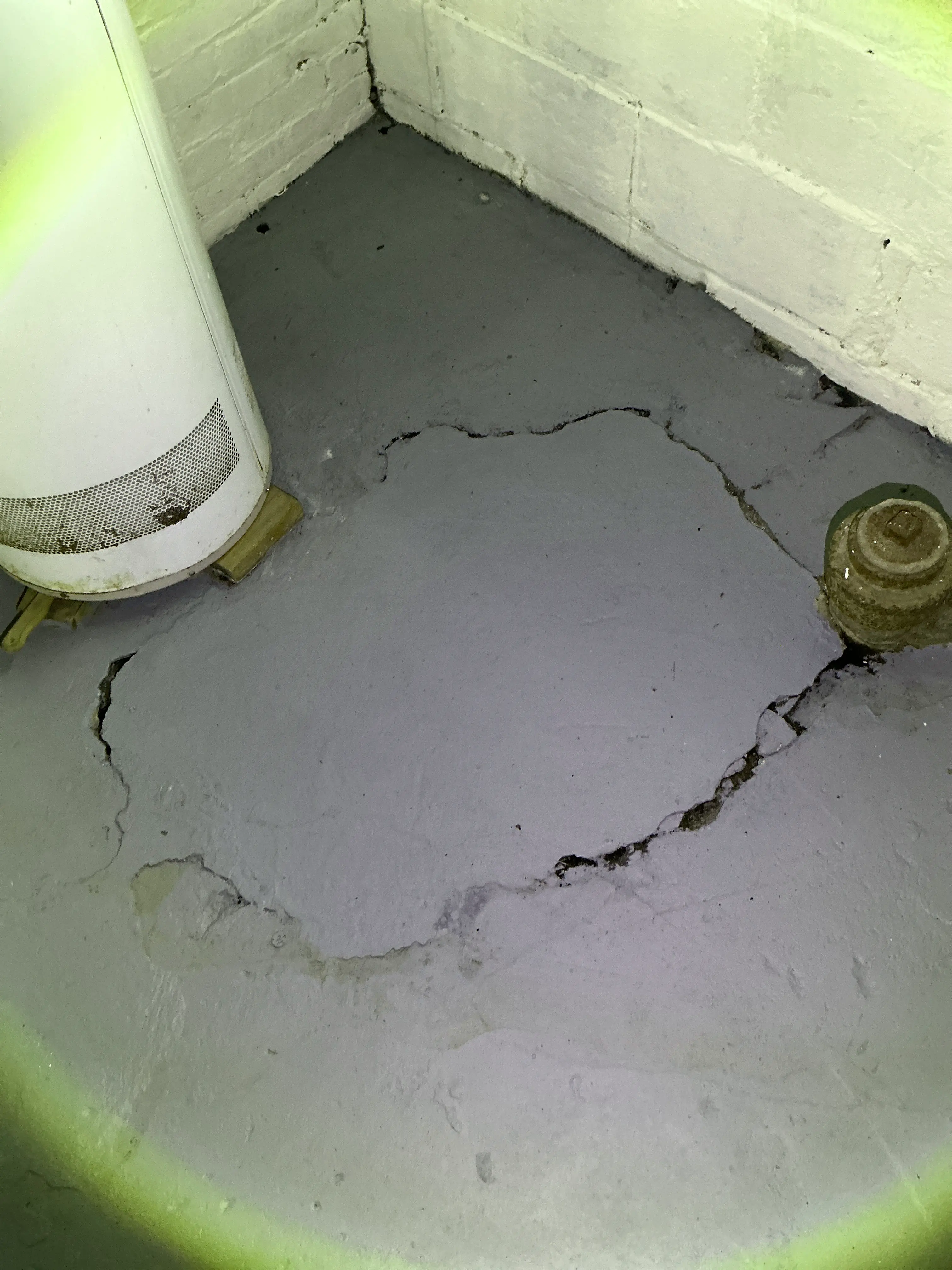 Large circular crack in concrete basement floor slab near a water heater and cleanout pipe 2026-08-02