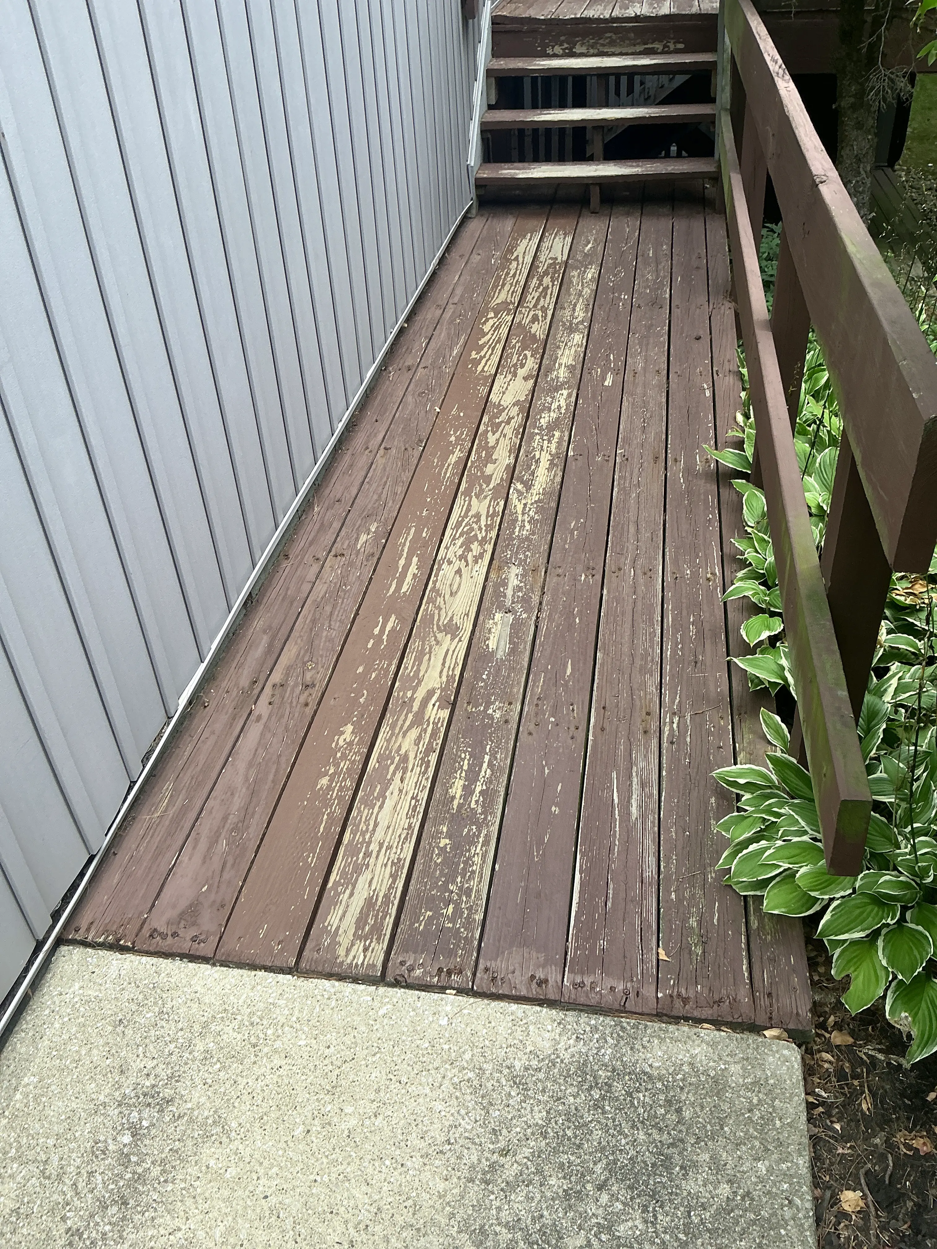 Peeling brown stain on wooden deck boards next to house siding 2026-09-02