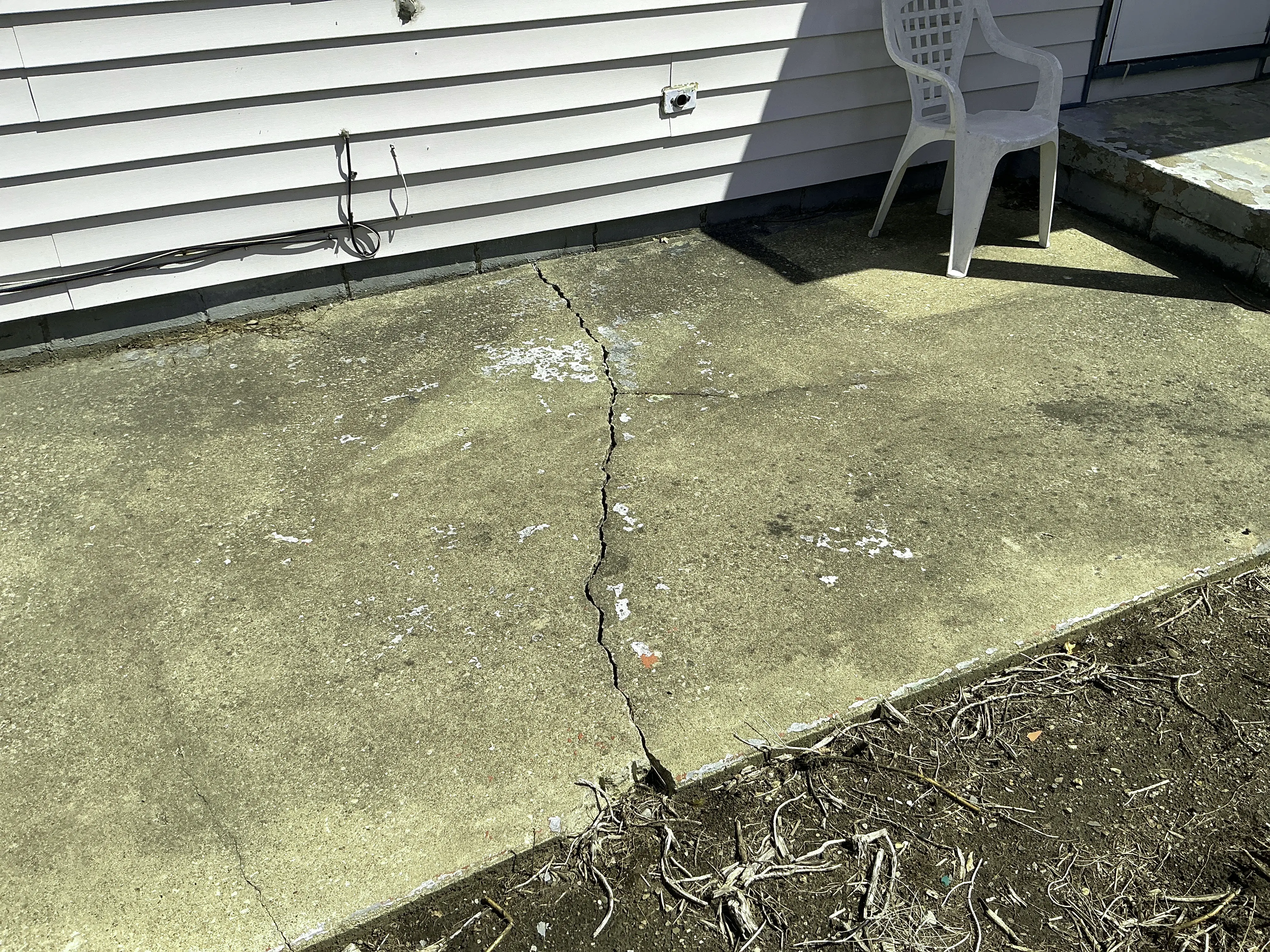 Large crack in concrete patio slab near house exterior siding 2026-08-18