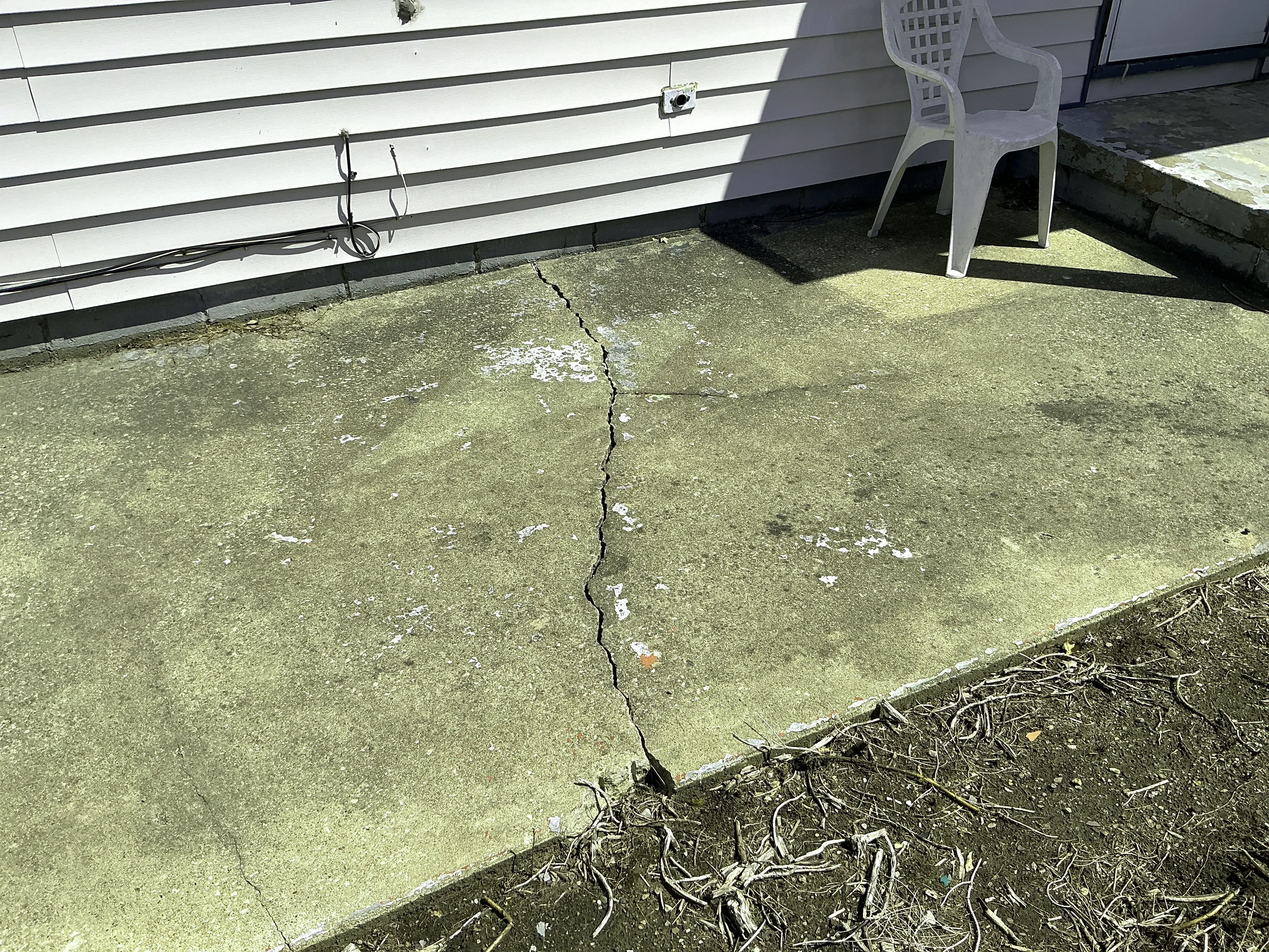 Large crack in concrete patio slab near house exterior siding 2026-08-03