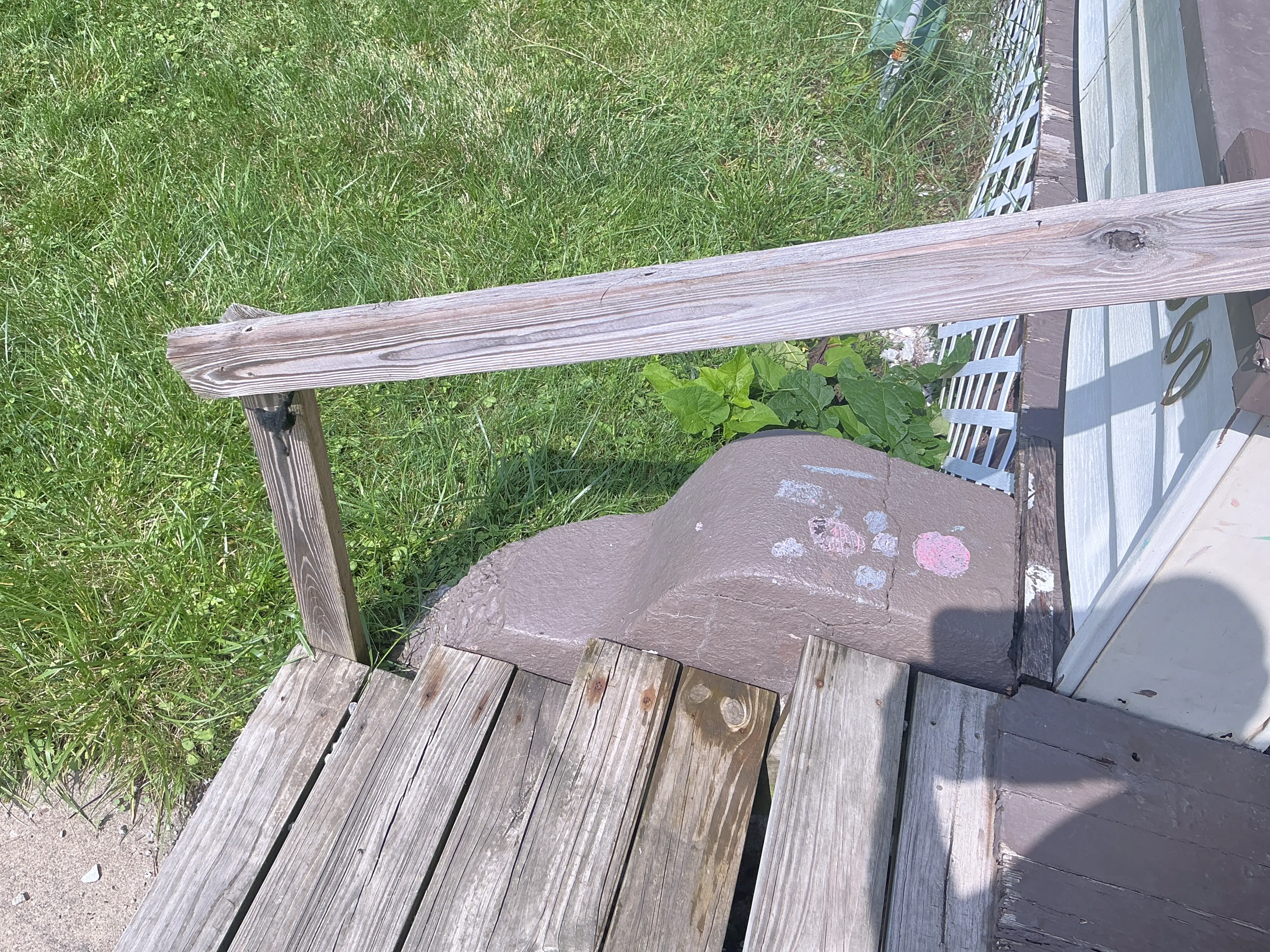 Weathered exterior wooden handrail and deck steps at a residential entry. 2026-07-25
