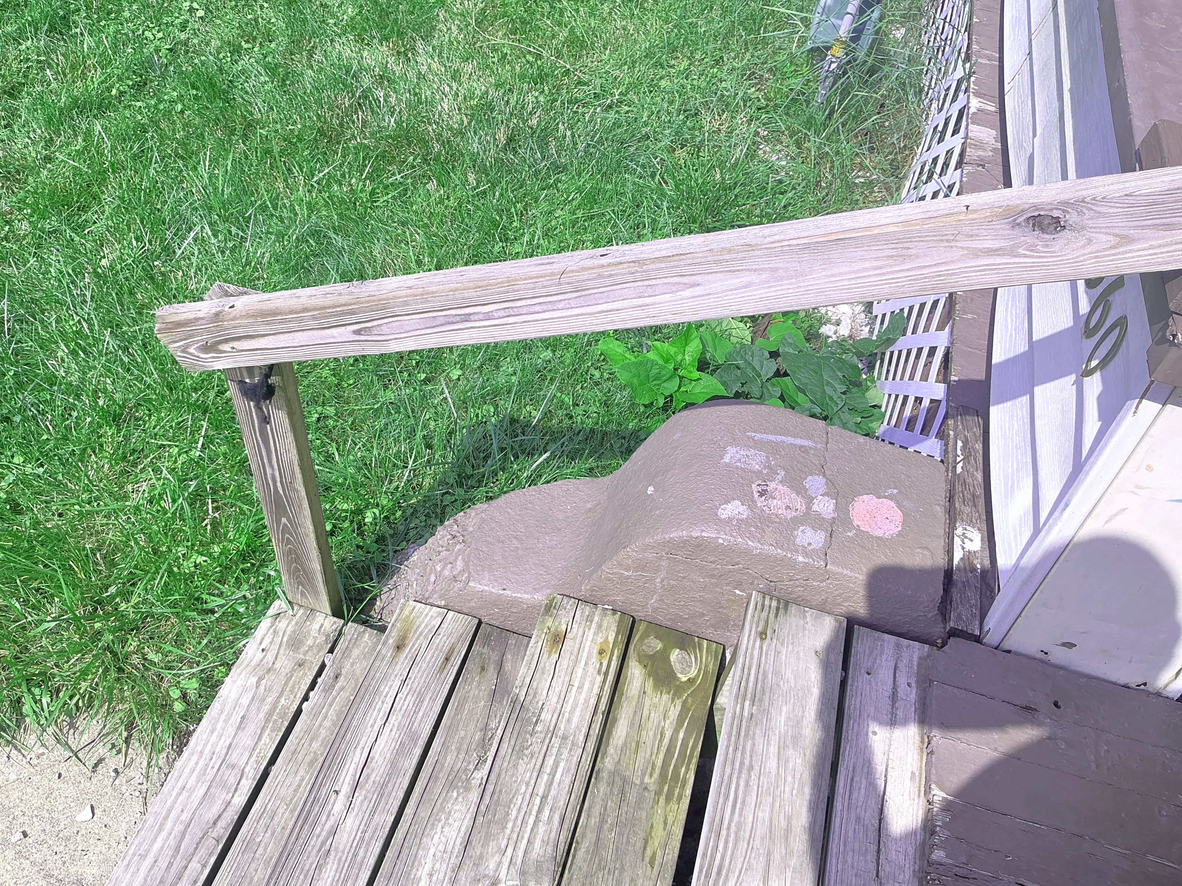 Weathered exterior wooden handrail and deck steps at a residential entry. 2026-09-01