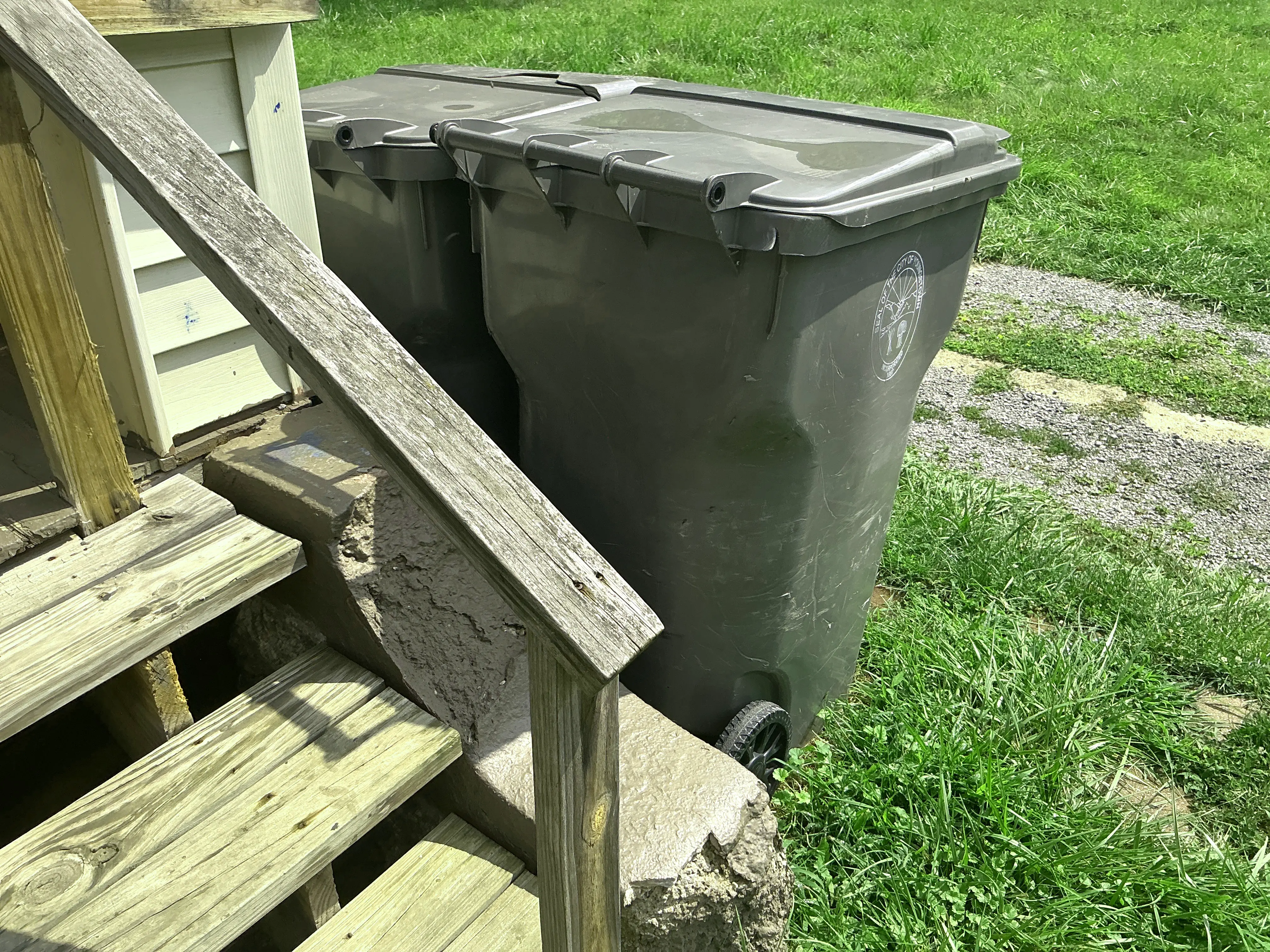 Exterior wooden porch stairs with handrail next to grey trash bins 2026-09-03