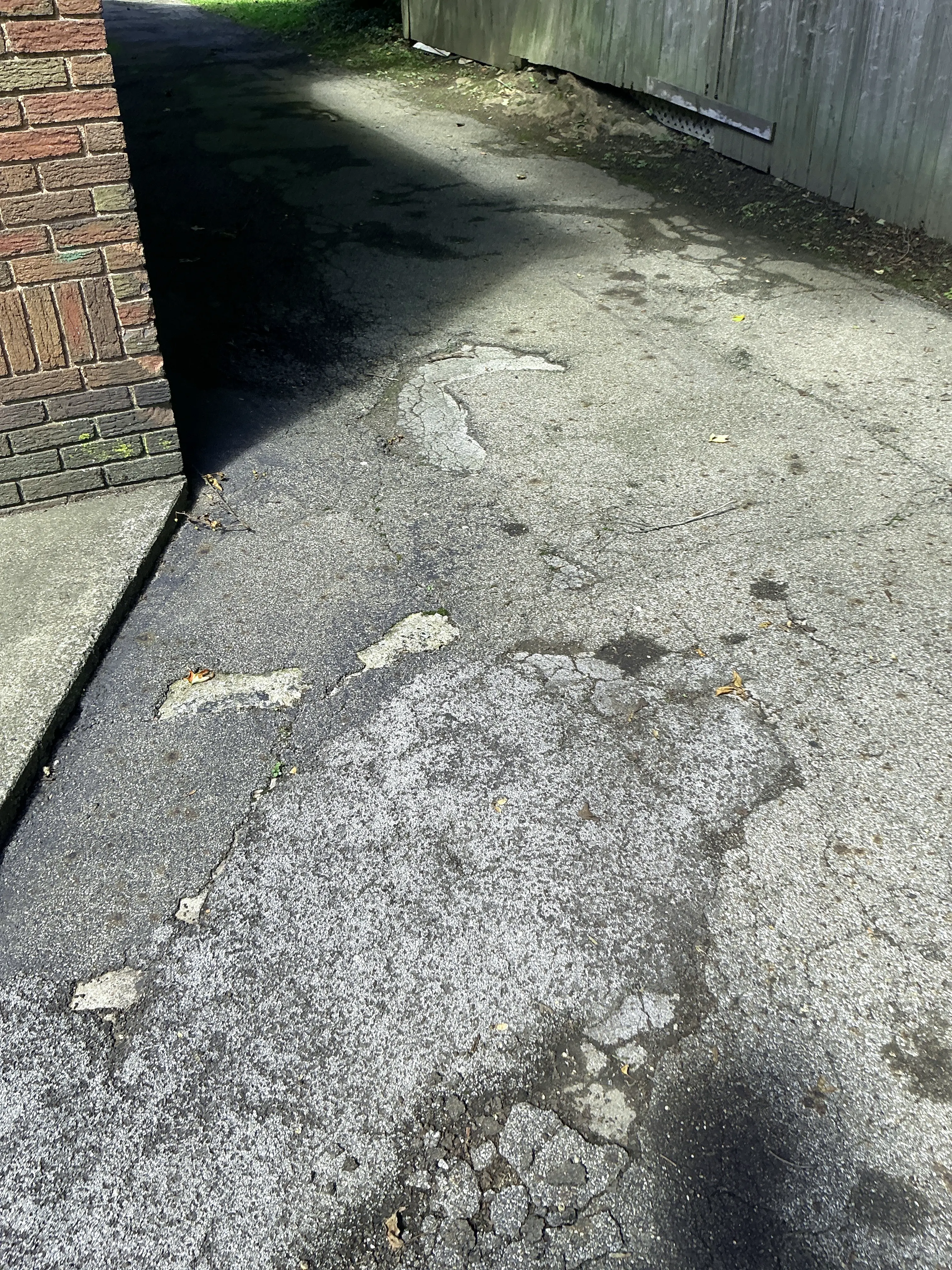 Cracked and worn asphalt driveway pavement with visible surface patches 2026-07-14