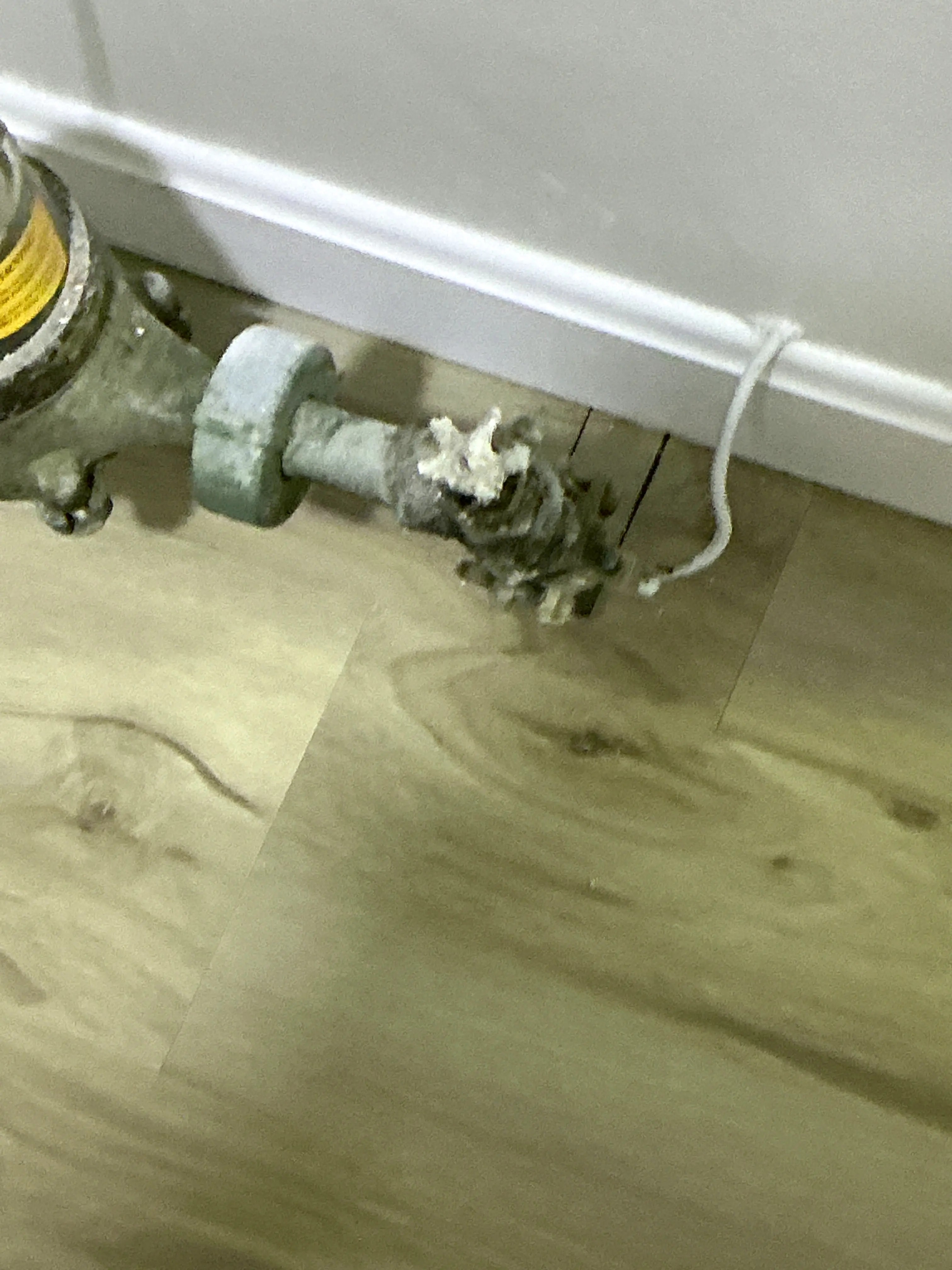 Corroded radiator valve near baseboard showing severe mineral buildup from leaking 2026-07-14